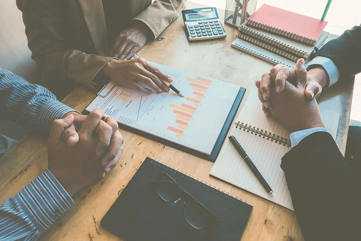 Two people discussing financial charts and using a calculator at a wooden table.